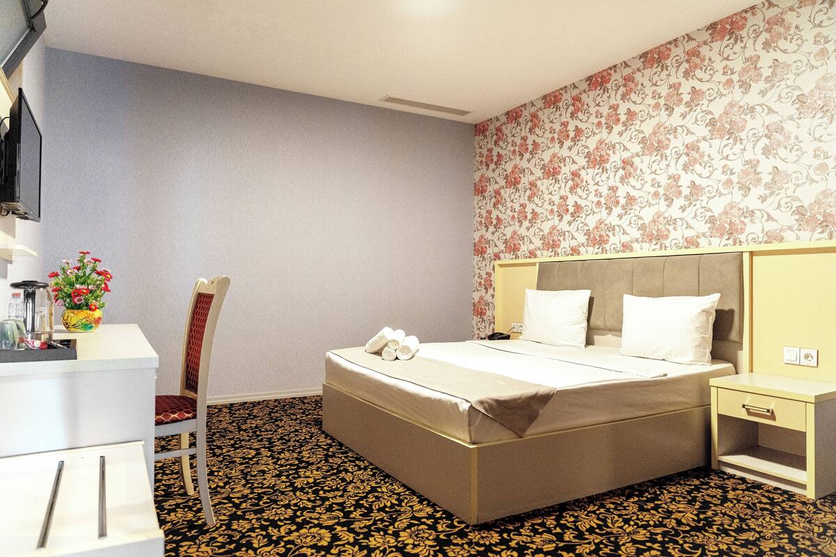 Habitación de hotel con cama, mesita de noche, silla y escritorio con un florero.