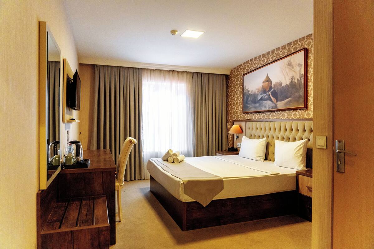 Una habitación de hotel con una cama, un escritorio con una silla, un televisor y un cuadro en la pared.