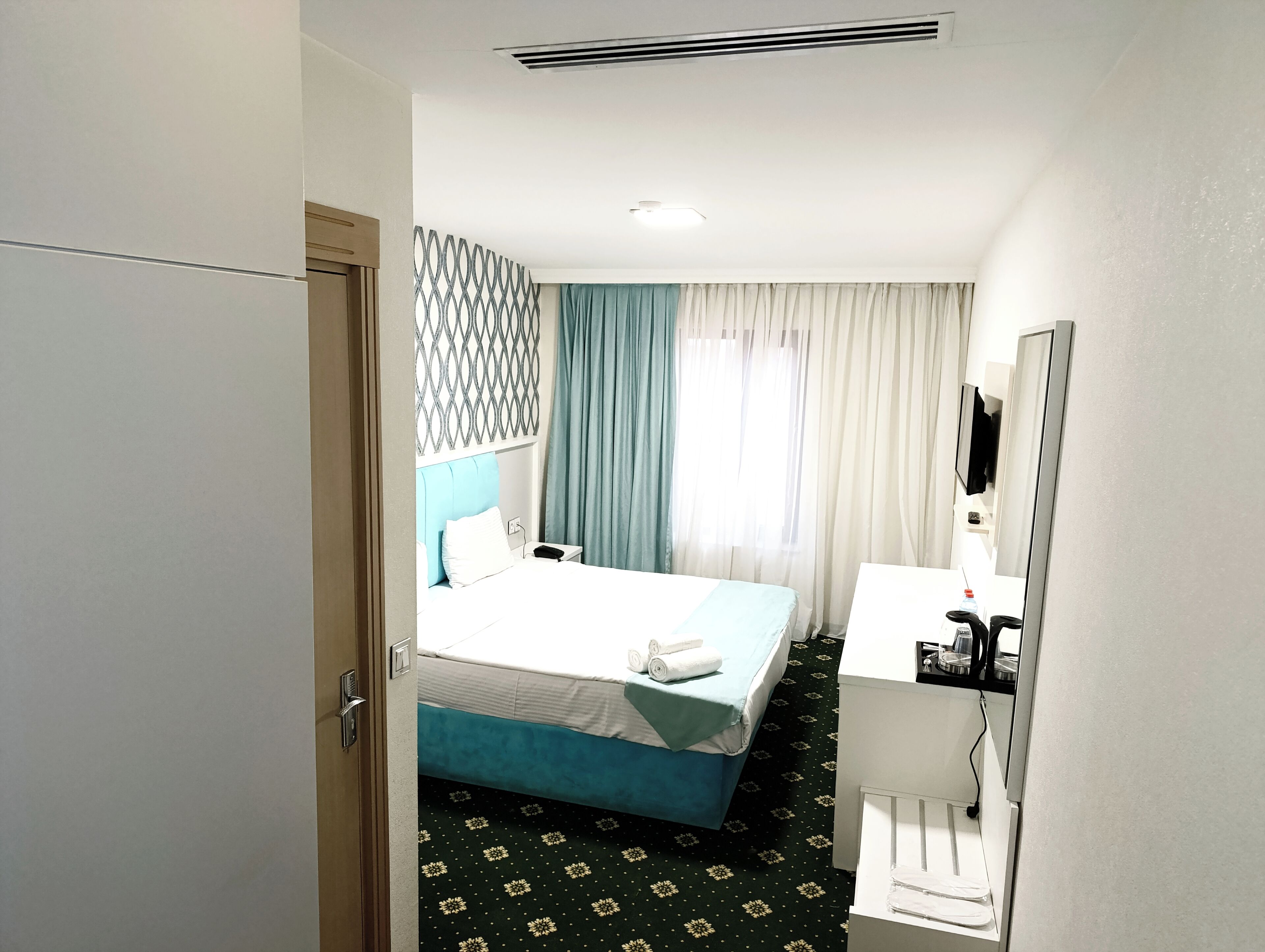 A hotel room with a bed, a desk, a mirror, and a window with curtains.