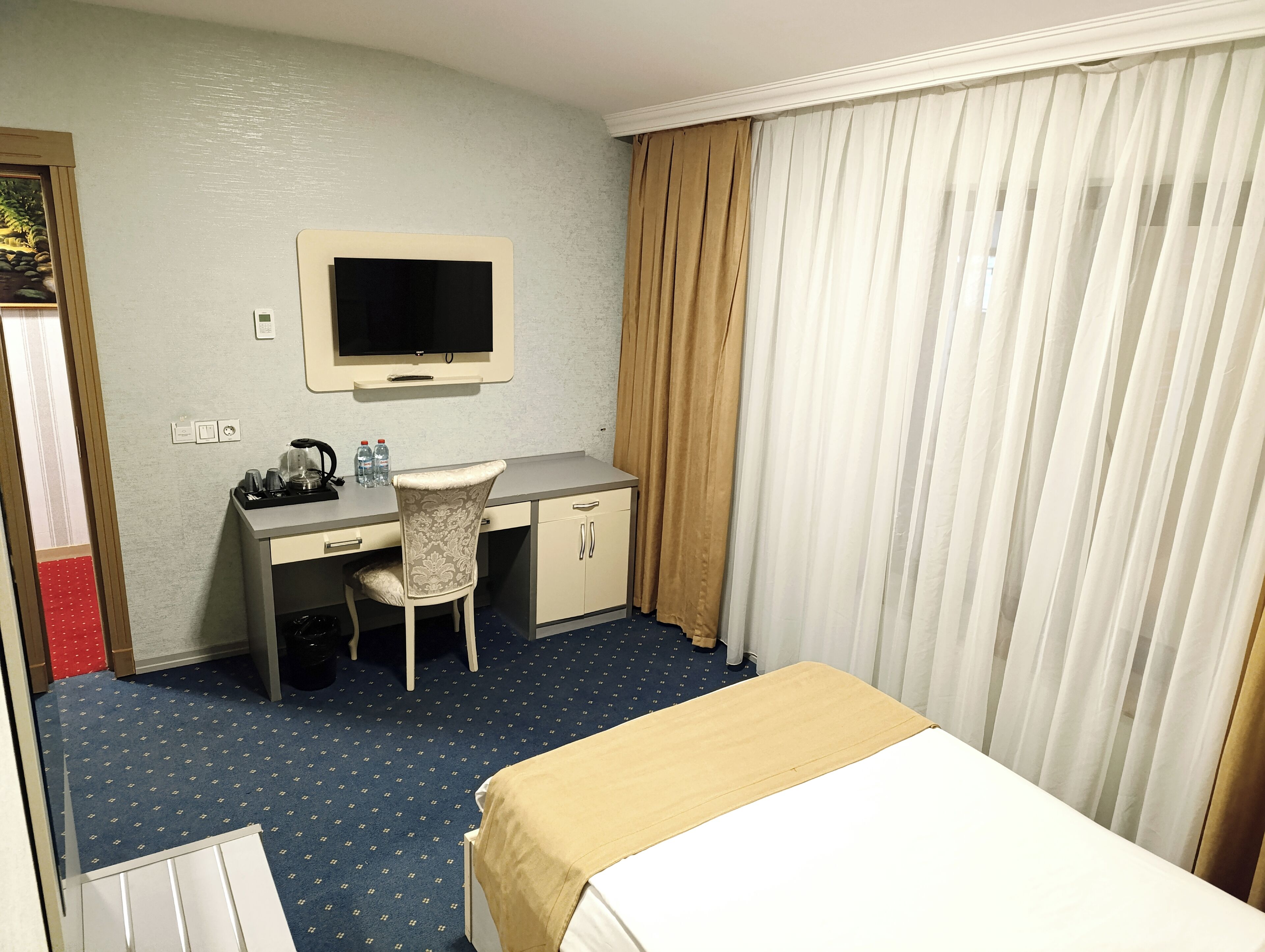 Une chambre d’hôtel équipée d’un lit, d’un bureau, d’une chaise, d’une télévision et de rideaux.