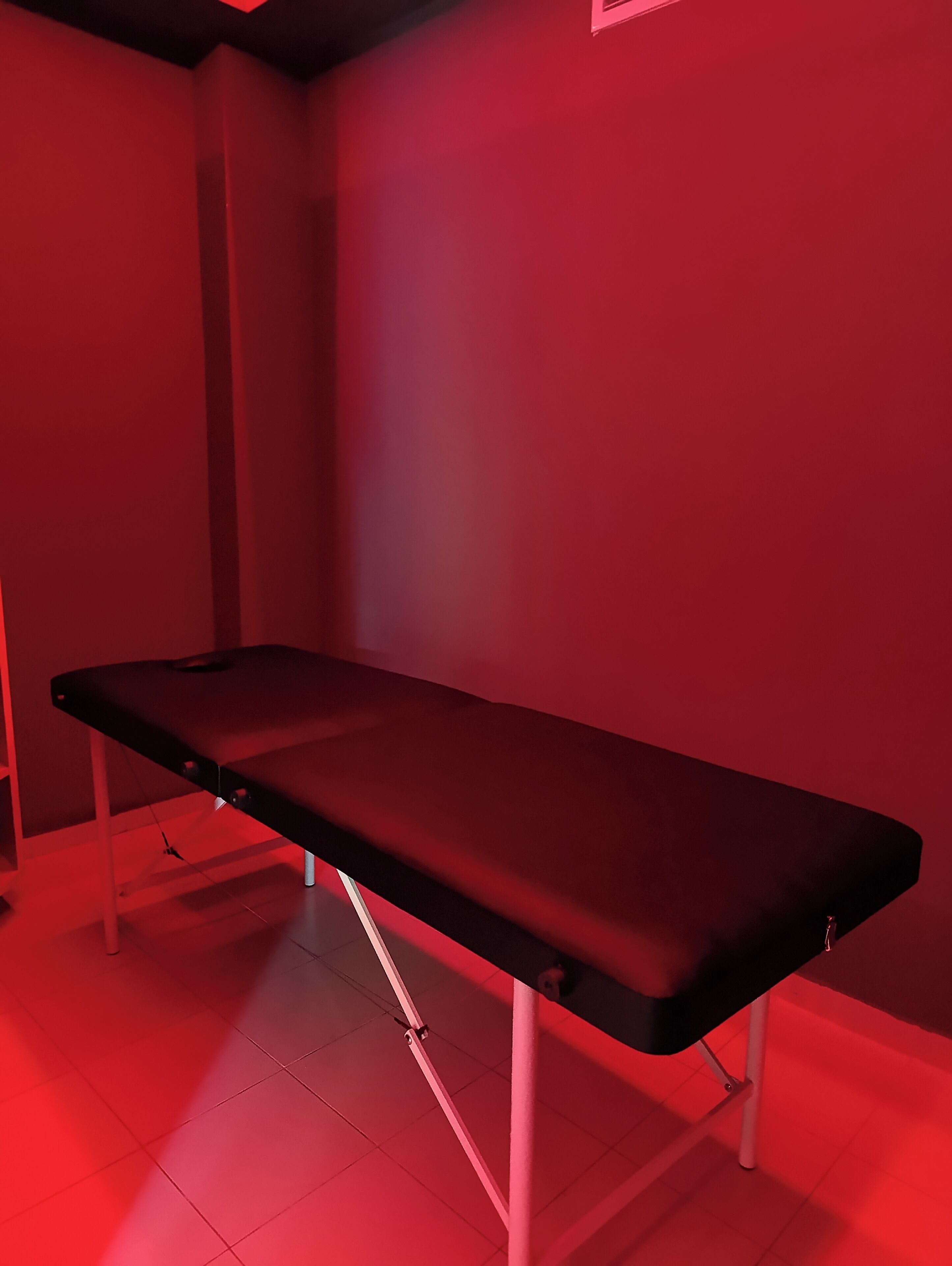 Une table d’examen éclairée de lumière rouge, dans une pièce aux murs blancs et au sol carrelé.