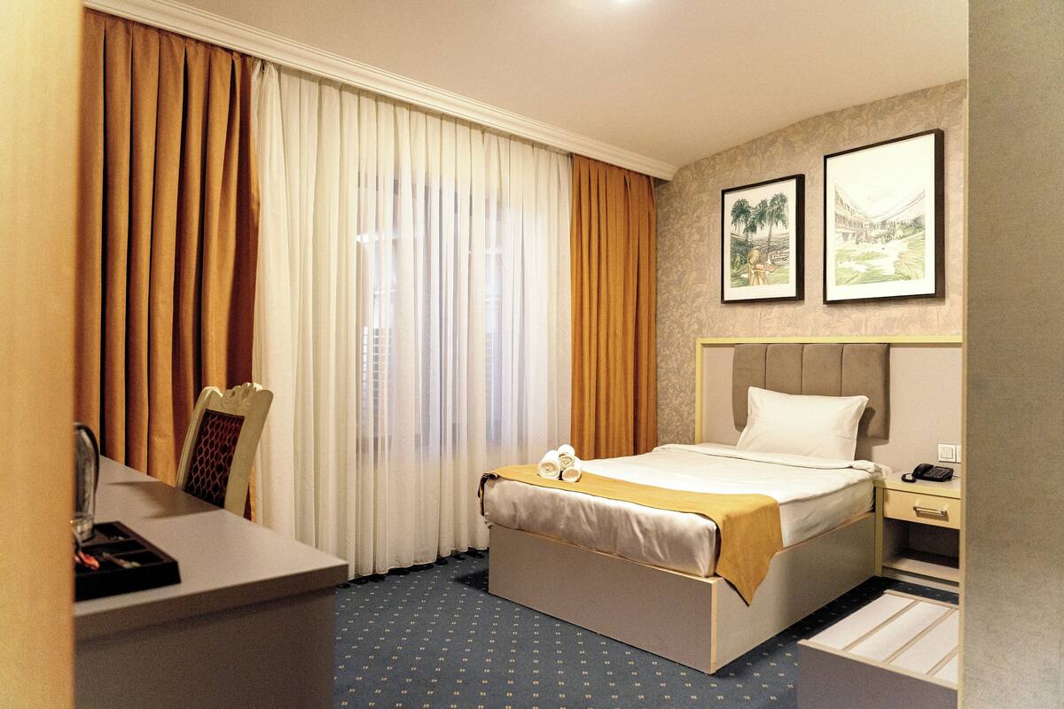 Habitación de hotel con cama, escritorio, silla, mesita de noche y dos cuadros en la pared.