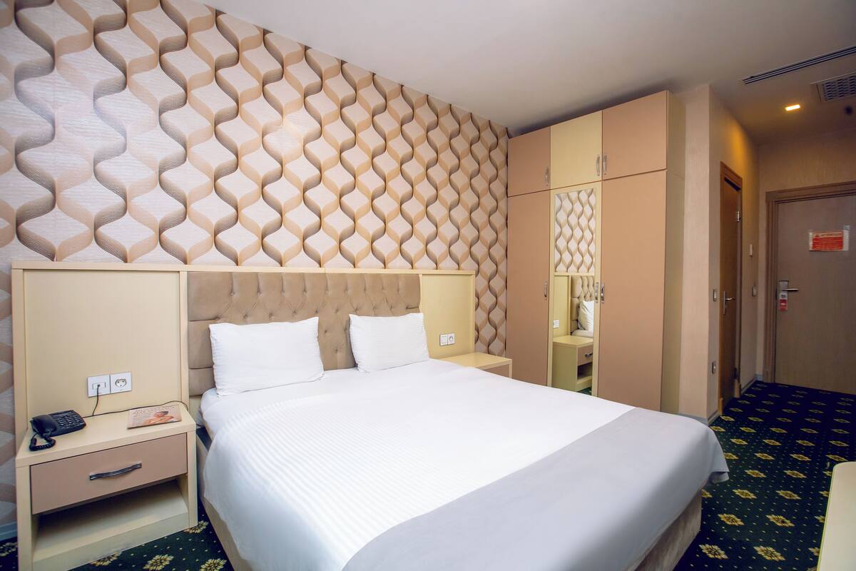 Una habitación de hotel con una cama grande, una mesita de noche, un armario y un espejo.