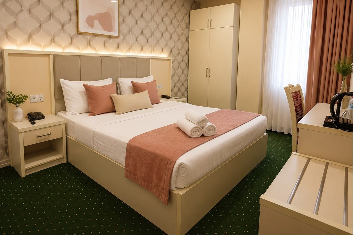 A hotel room with a bed, bedside tables, a wardrobe, and a desk with a chair.