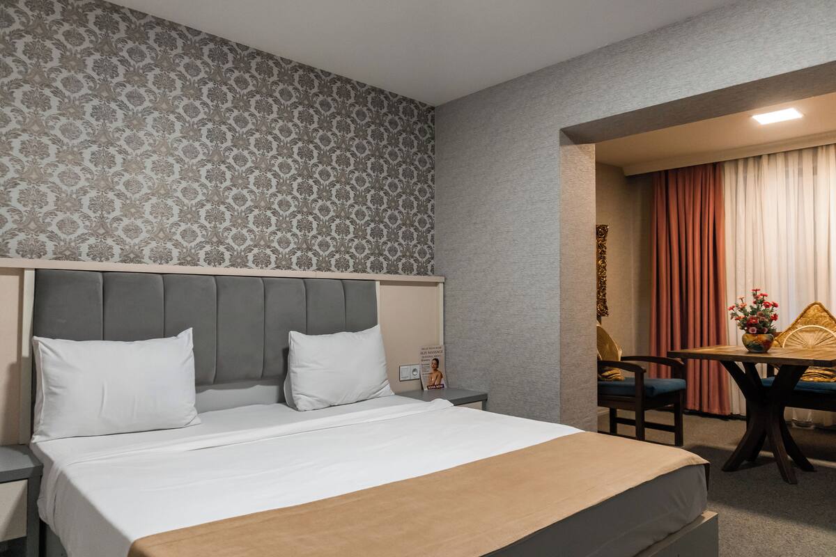 Habitación de hotel con cama, mesitas de noche, un escritorio con silla y papel tapiz estampado.