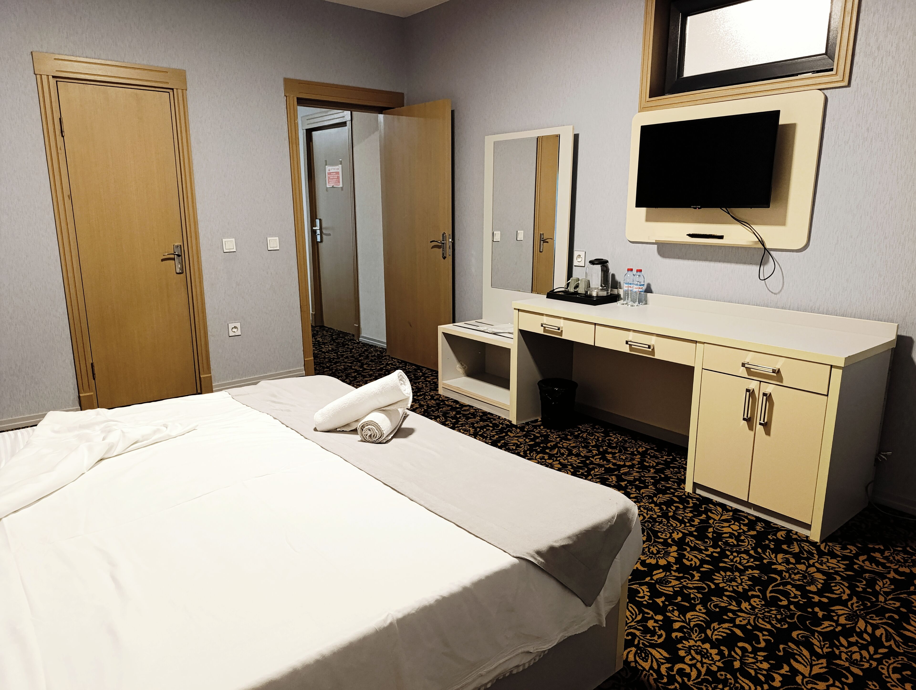 Une chambre d’hôtel comprenant un lit, un bureau avec un miroir, une télévision et une poubelle.