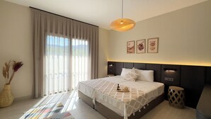 Camera moderna con un ampio letto, una lampada da comodino e vista sull'esterno attraverso tende leggere.