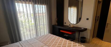 A bedroom with a bed, a desk, a mirror, and a hanging light fixture.