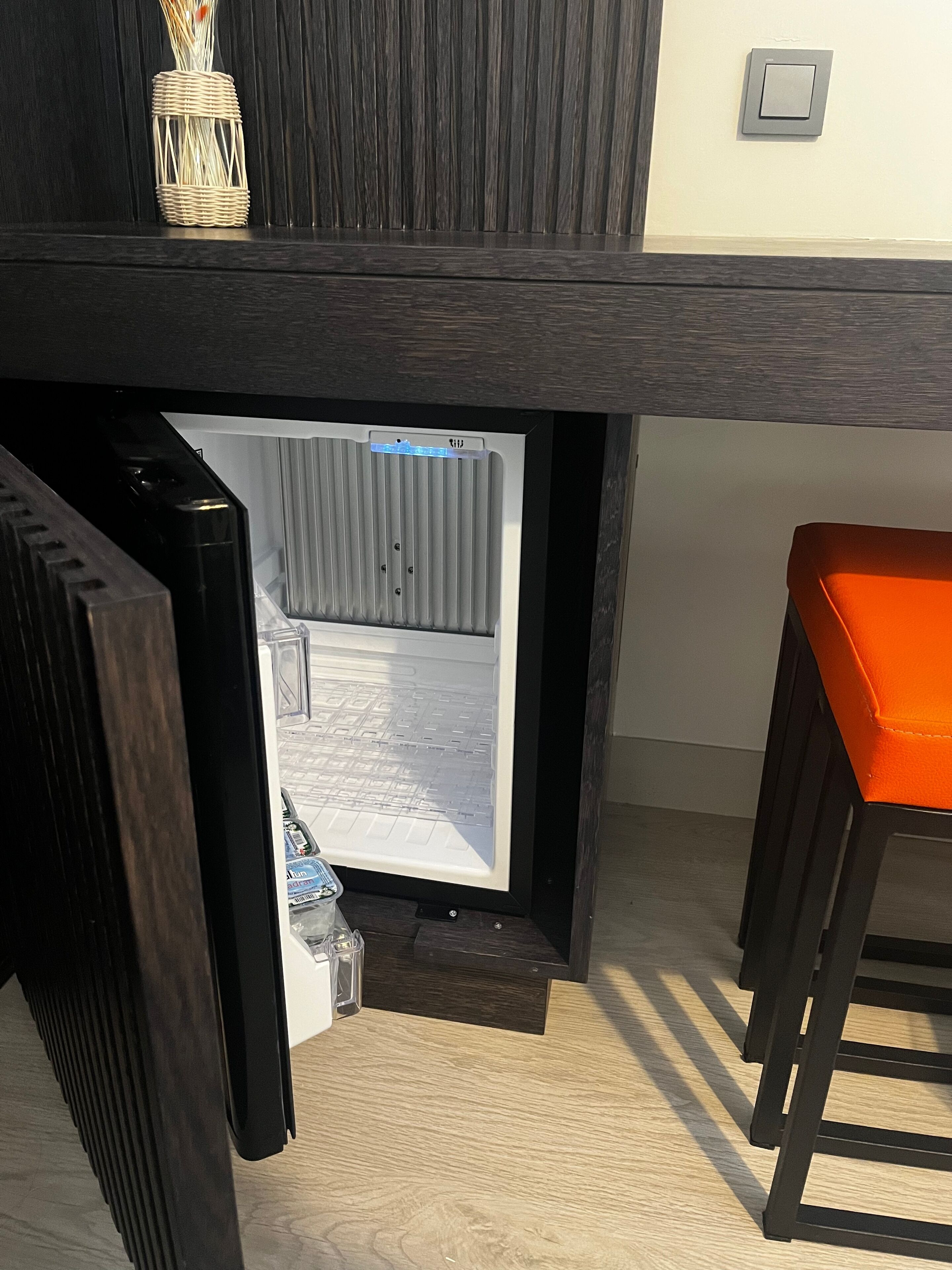 Una habitación con refrigerador integrado, una pequeña mesa con un recipiente de vidrio y suelo de madera.