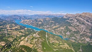 Un paysage montagneux, avec une rivière sinueuse, un ciel dégagé et un mélange de zones boisées et de champs ouverts.