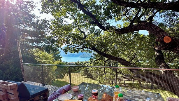 Un espacio al aire libre con mesas dispuestas para una comida, rodeado de árboles y vistas al paisaje.
