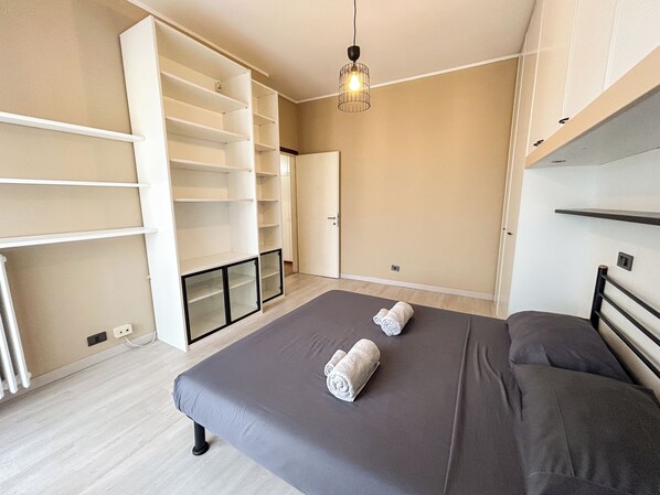 A bedroom with a bed, two rolled towels, a wardrobe, and a hanging light fixture.
