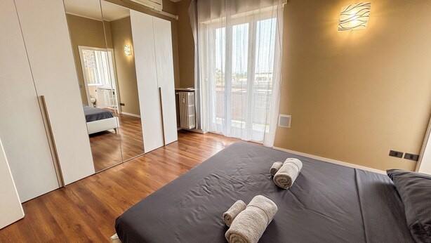 A bedroom with a large bed, a wardrobe, a radiator, and a window with curtains. - SkyLoft Bergamo - Chic Penthouse with Unique Panorama (Bergamo)