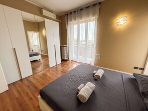 Quarto com cama grande, guarda-roupa, radiador e janela com cortinas.