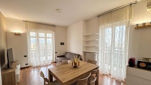 A spacious living room with a wooden dining table, two chairs, a sofa, and a TV. - SkyLoft Bergamo - Chic Penthouse with Unique Panorama (Bergamo)