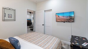 Un dormitorio con cama, televisión, maleta y puerta que da a otra habitación.