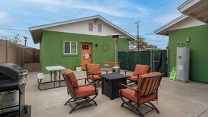 Eine Terrasse mit Gartenmöbeln, einem Grill und einem Gewächshaus im Hintergrund.