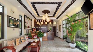 A hotel lobby with a reception desk, a sofa, a coffee table, and a large potted plant. - Superior King room - Hoi An Discovery Villa (Cam Chau ward)