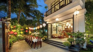 A restaurant with outdoor seating, palm trees, and string lights. - Superior King room - Hoi An Discovery Villa (Cam Chau ward)