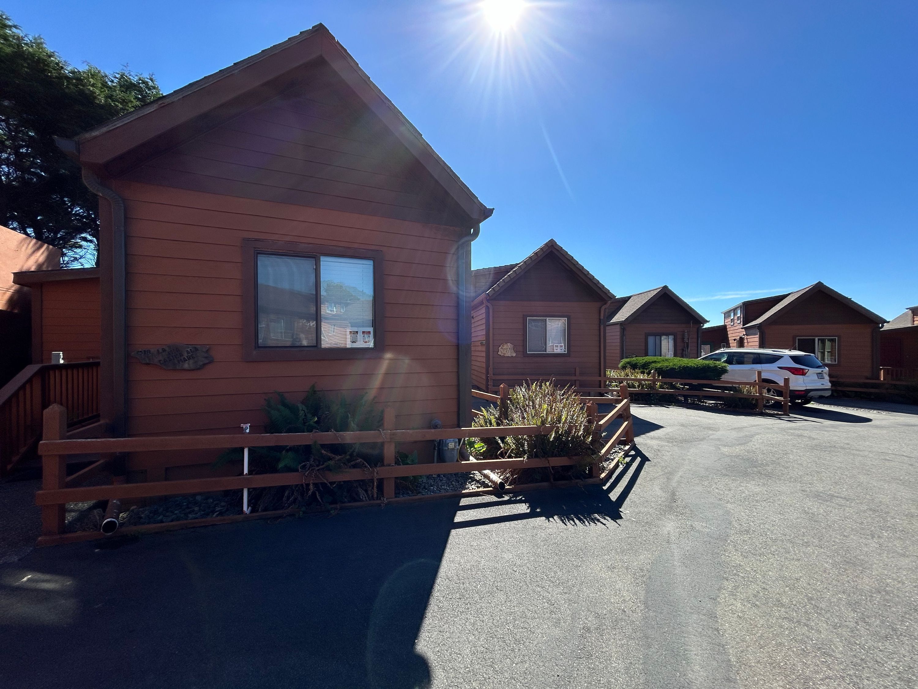 A row of wooden cabins with a clear sky and a parked car in front.