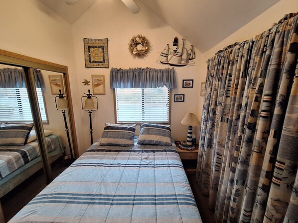 A bedroom with a bed, a mirror, a lamp, a window with blinds, and curtains. - Luxurious Oceanfront Cabin 7 Getaway w Hot Tub (Smith River)