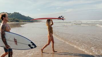 Two people walking on a beach, one carrying a surfboard.