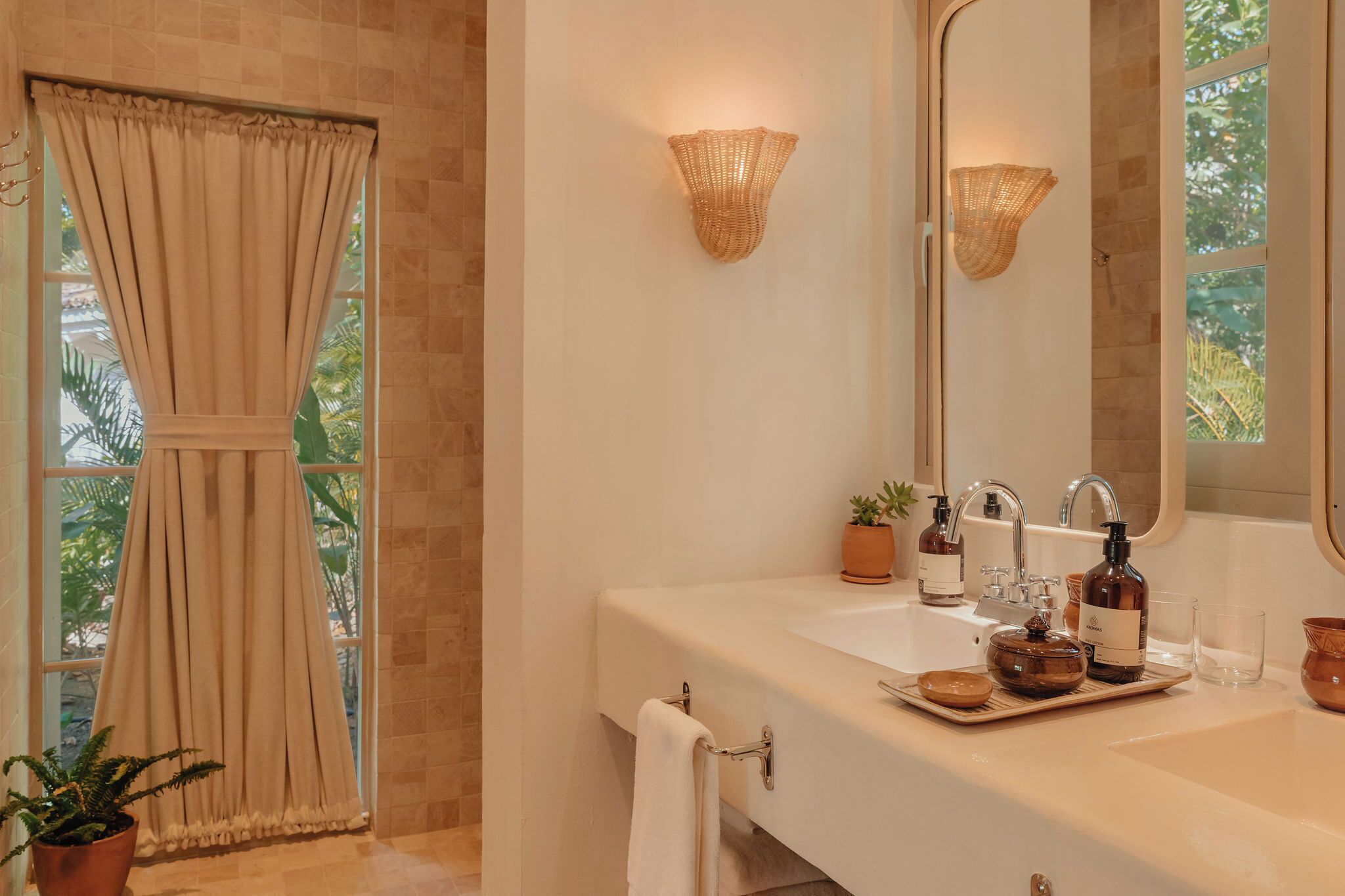 A bathroom with a large mirror, two sinks, a towel rack, and a window with curtains.