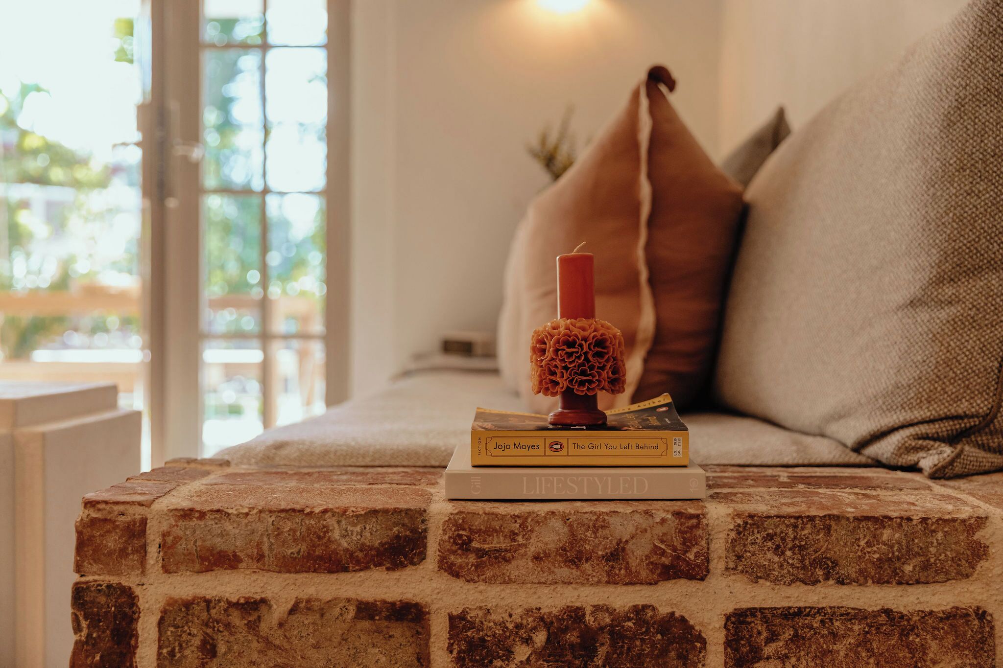 A brick wall, a candle, and books on a table.