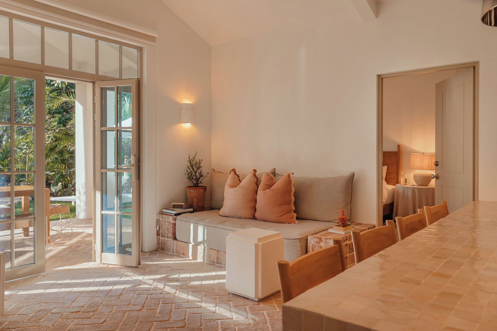Una habitación amplia con un gran comedor, un sofá con cojines, una planta en maceta y un ventanal corredero que da a un espacio exterior.