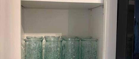 Ein Küchenschrank mit zwei Einlegeböden, einer mit klaren Glasbehältern und der andere mit grünen Glasbehältern.