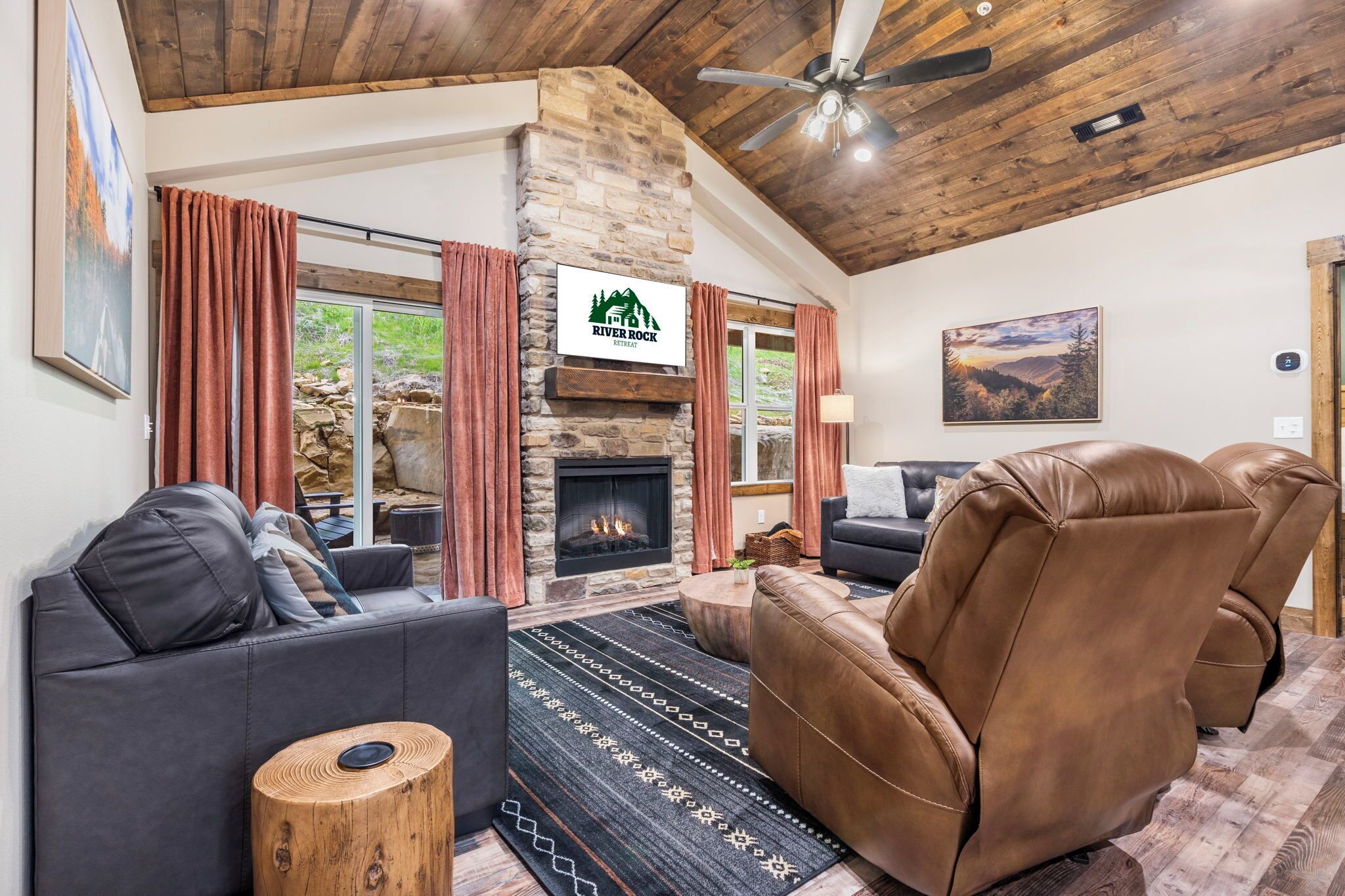 A cozy living room with a stone fireplace, leather sofas, and a large window with curtains.