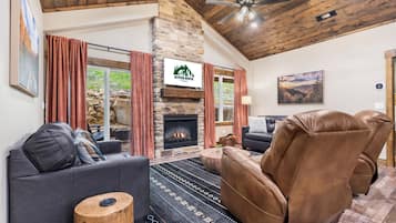 A cozy living room with a stone fireplace, leather sofas, and a large window with curtains.