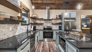 Une cuisine moderne avec un mur de fond en briques, des appareils électroménagers en acier inoxydable et des poutres en bois au plafond.