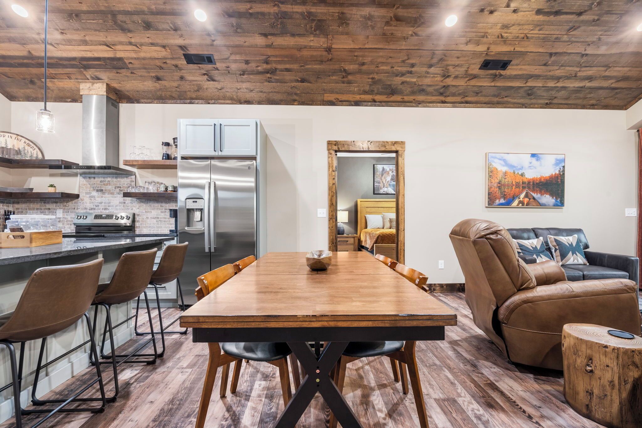 A modern kitchen with stainless steel appliances, a wooden dining table with chairs, and a cozy seating area with a leather sofa and a coffee table.