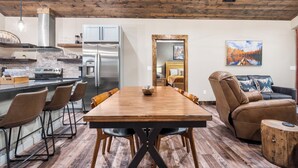 Une cuisine moderne équipée d’appareils électroménagers en acier inoxydable, une table à manger en bois avec des chaises, et un coin salon confortable avec un canapé en cuir et une table basse.