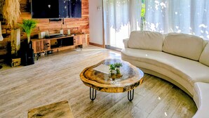 Un salón moderno con pared de madera, un televisor de pantalla plana grande, un sofá blanco y una mesa de centro redonda.