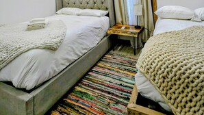 Habitación de hotel con dos camas, alfombra a rayas colorida, unidad de aire acondicionado, un cuadro en la pared y una lámpara de techo original.