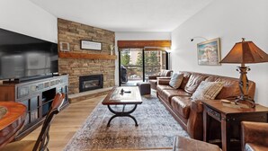 Un salon avec une cheminée en pierre, un canapé en cuir, une table basse en bois et un téléviseur posé sur un meuble.