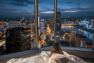 Una persona acostada en la cama con vistas a un paisaje urbano a través de amplias ventanas.