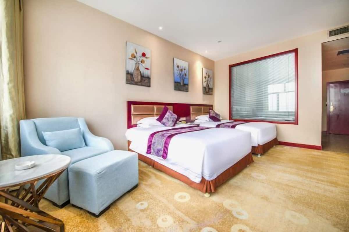 A hotel room with two beds, a sitting area with a chair and table, and artwork on the walls.