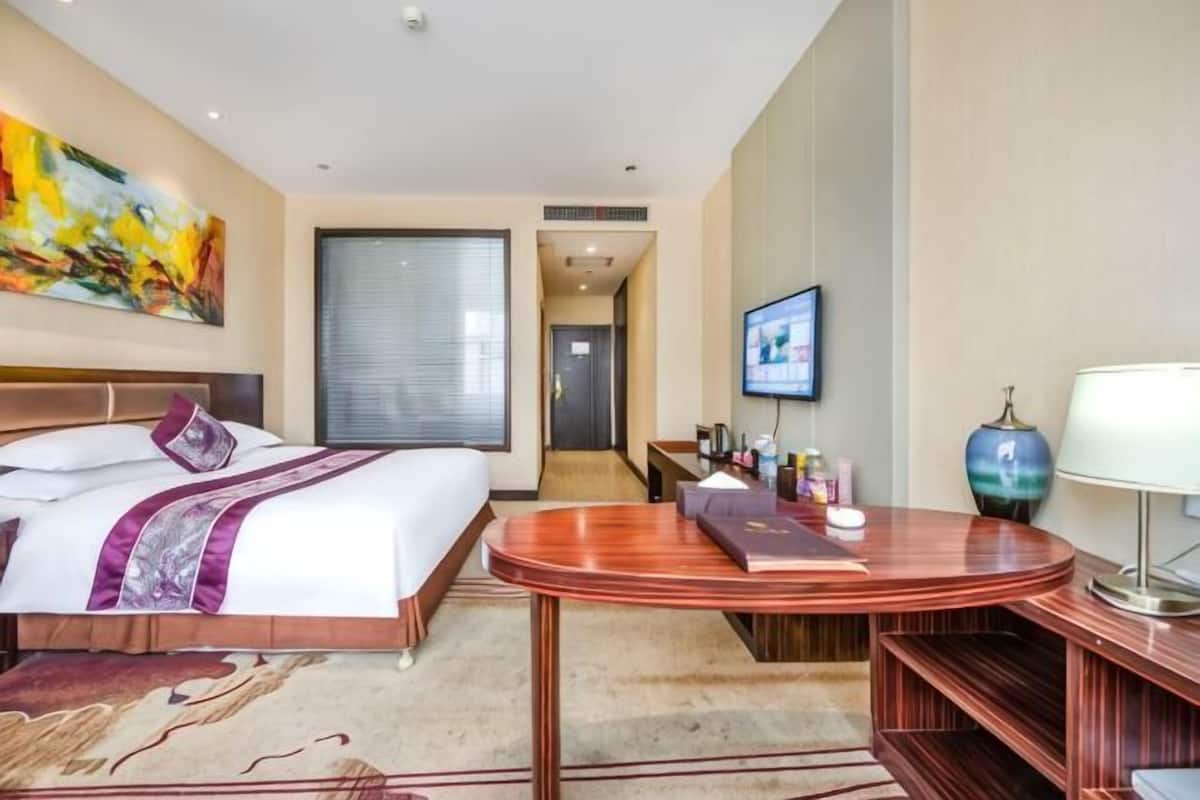 A hotel room with a bed, a desk, a chair, a TV, and a large window.