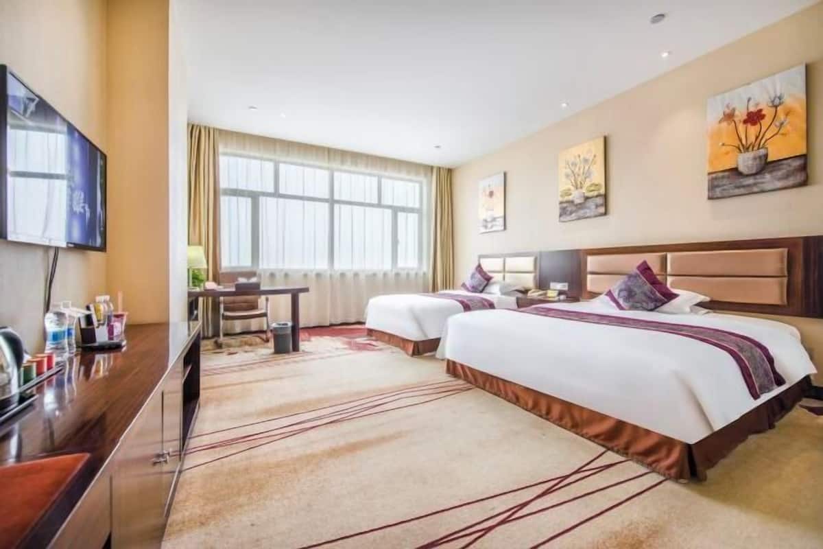 A hotel room with two beds, a desk, a TV, and artwork on the walls.