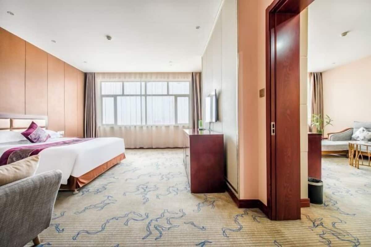 A hotel room with a bed, a desk, a chair, a TV, and a large window.