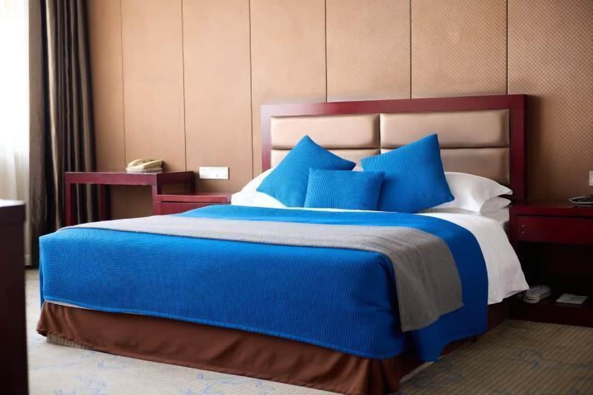 A hotel room with a large bed, a wooden headboard, a nightstand, and a desk.