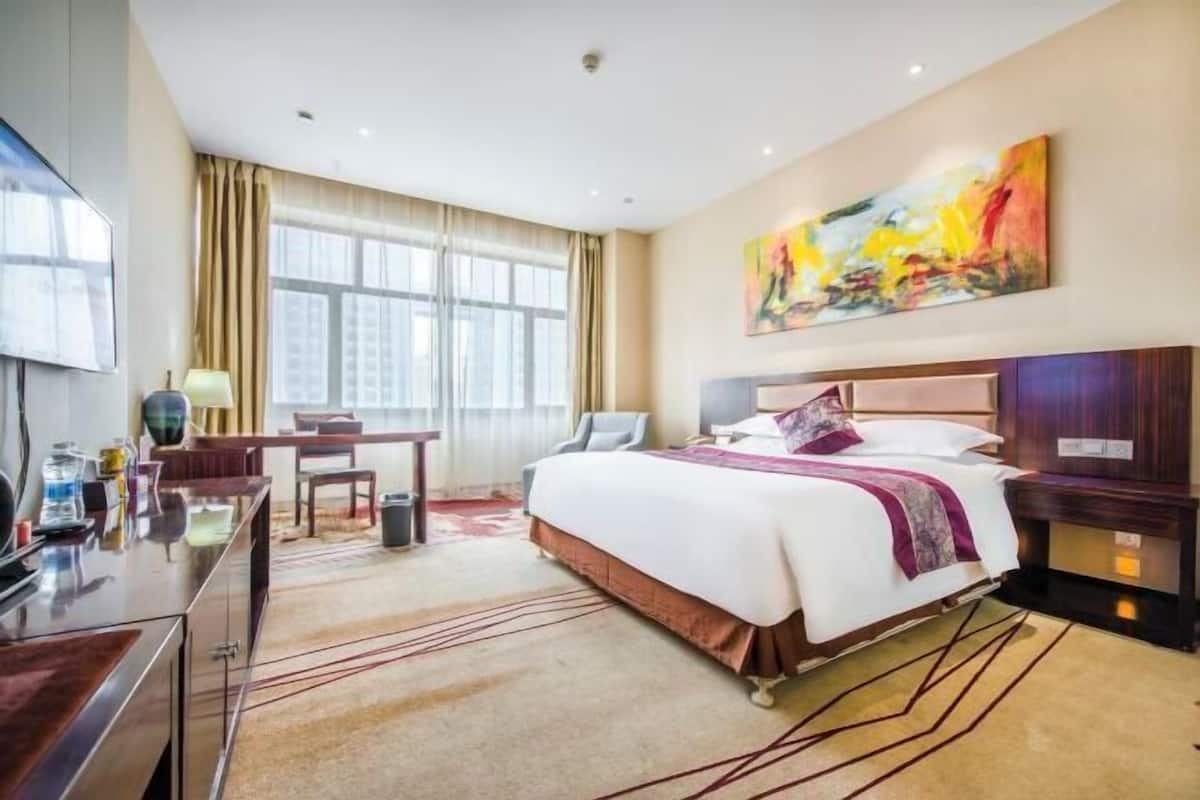 A hotel room with a bed, a desk, a chair, a TV, and a painting on the wall.