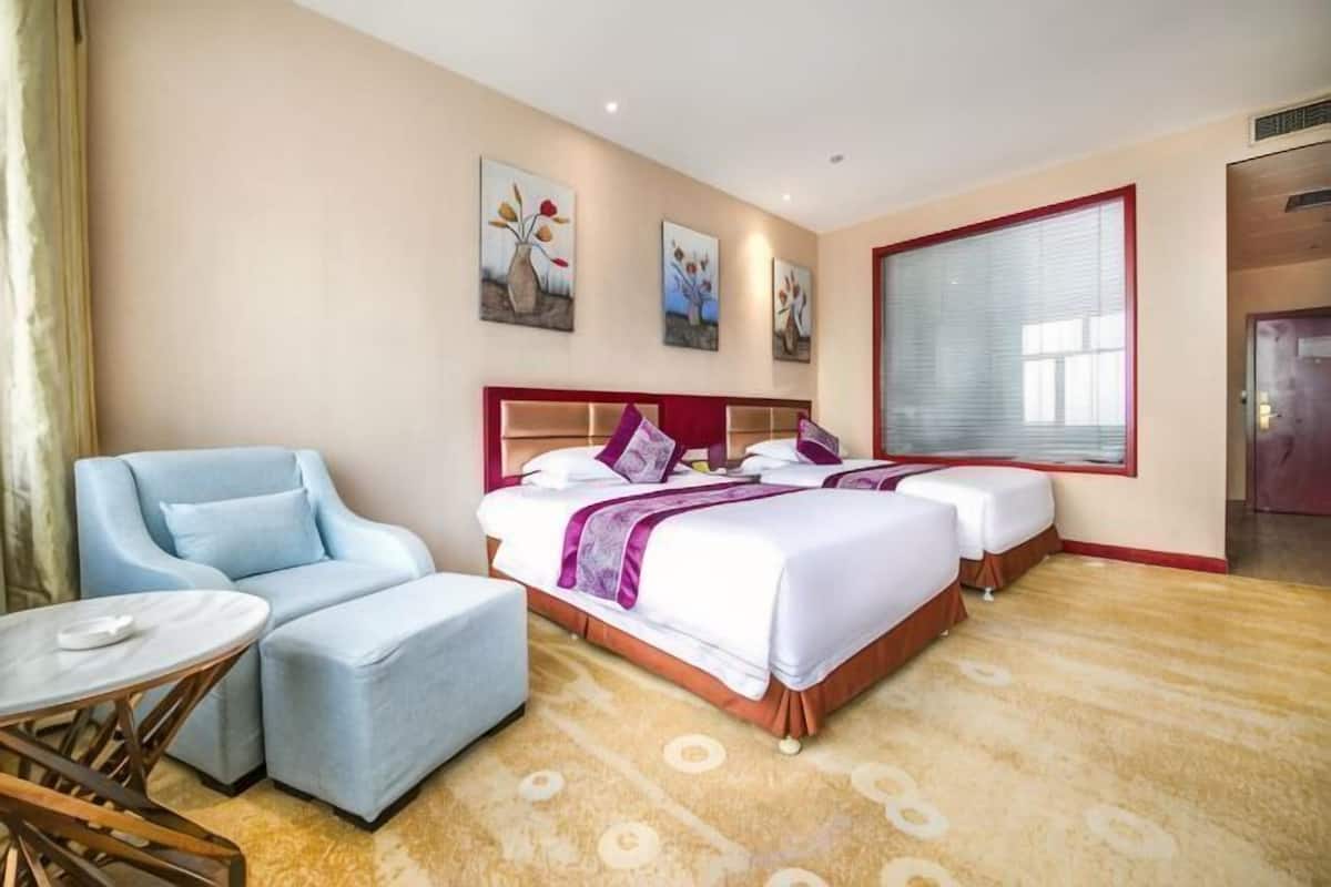 A hotel room with two beds, a sitting area with a chair and table, and artwork on the walls.