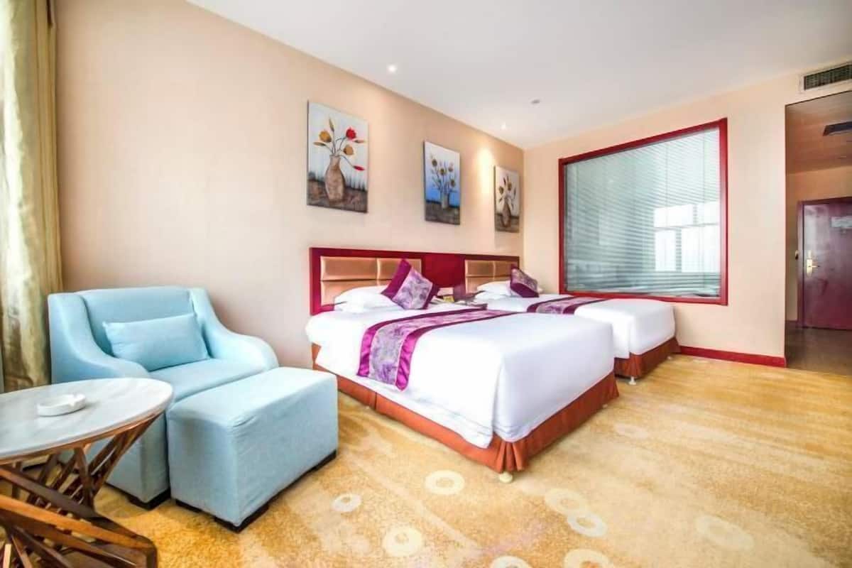 A hotel room with a bed, two bedside tables, a chair, a small table, and artwork on the walls.