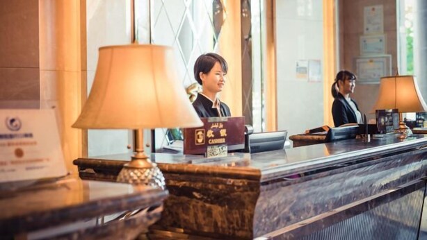A hotel reception desk with a cash register, a lamp, and a framed certificate on the wall. - Minghua Hotel (Aksu Tianbai Fashion Shopping Center Xinglong Underground Street Branch) (Aksu City)