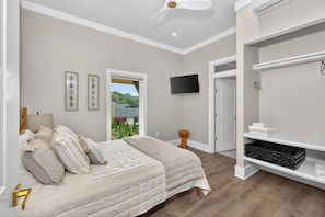 A bedroom with a bed, a television, a wardrobe, and a window with a view of greenery.