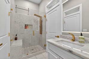 A modern bathroom with a glass-enclosed shower, marble tiles, and gold fixtures.